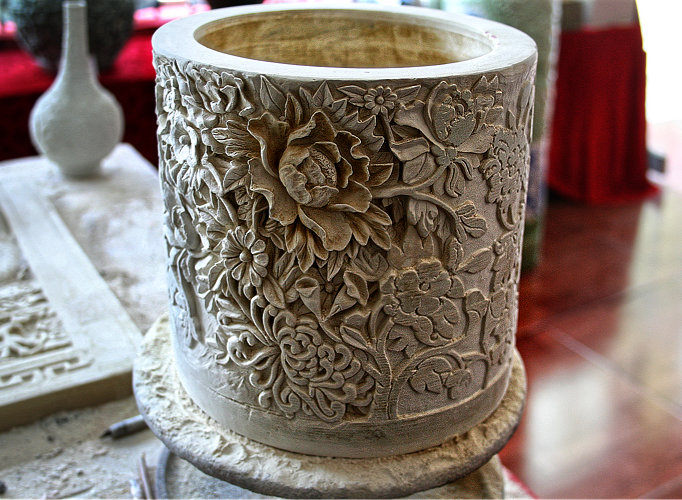 Reich beschnitztes Gefäß. Die dicke Wandung ist übersät mit ornamentalen Blumen– und Pflanzenmotiven.