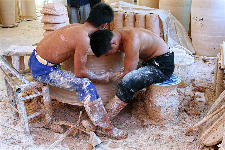 Dreher in Jingdezhen. Die beiden drehen die gewaltigen Ringe für spätere Monumentalvasen, die aus diesen Ringen zusammengesetzt werden. Es geht um enorme Tonmassen. Der eine packt die Handgelenke des anderen, um dessen Händen mehr Druck zu verleihen.